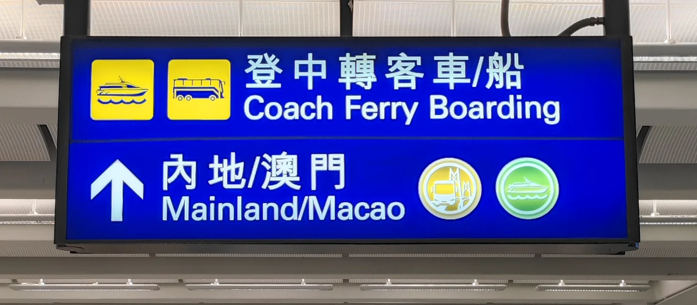 Blue Hong Kong Airport sign pointing toward Coach Ferry Boarding and Mainland/Macao